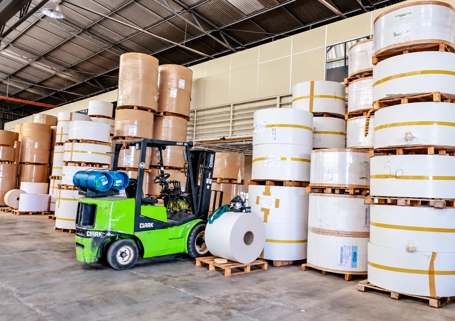 Estoque de bobinas de papel e empilhadeira na fábrica da Grifo